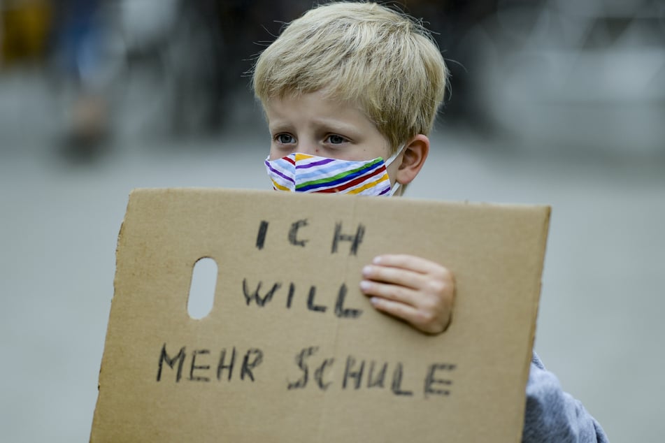 Ein Junge trägt einen Mund-Nasenschutz, während er ein Stück Pappkarton mit der Aufschrift "Ich will mehr Schule" auf dem Gänsemarkt vor sich hält.