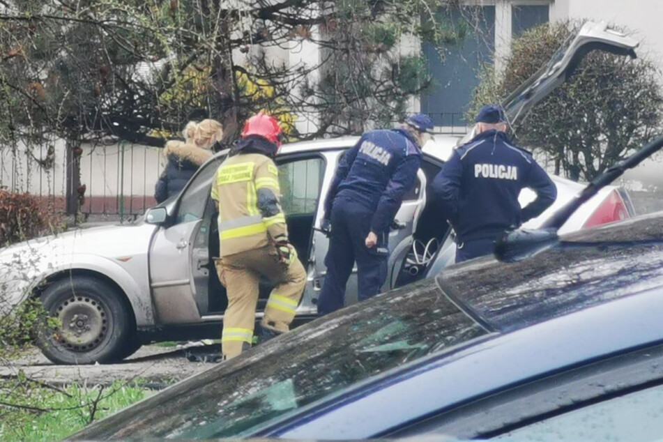 Polizisten und ein Feuerwehrmann begutachten das teilweise verbrannte Auto.