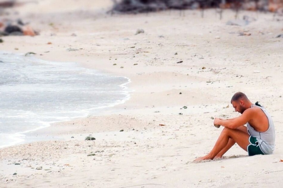 Nachdenklich sitzt der 25-Jährige am Strand.