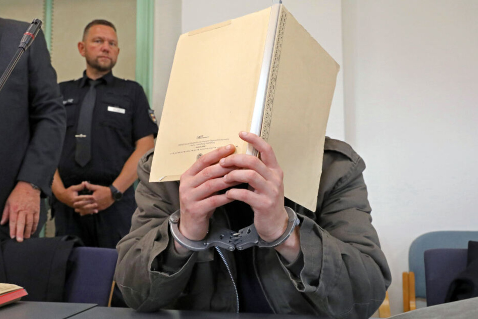 Der angeklagte Stiefvater hält sich eine Mappe vor das Gesicht.