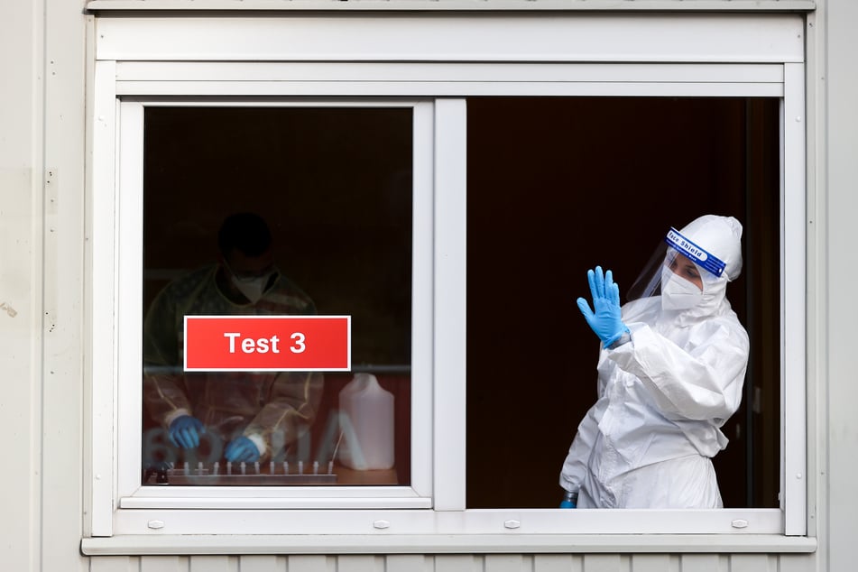 Sachsen, Augustusburg: Eine Frau in Schutzkleidung winkt Testwillige zu ihrem Fenster an einem Testcenter. Nach Ostern sank die Inzidenz in Deutschland leicht. Doch vielerorts wurden weniger Tests durchgeführt.