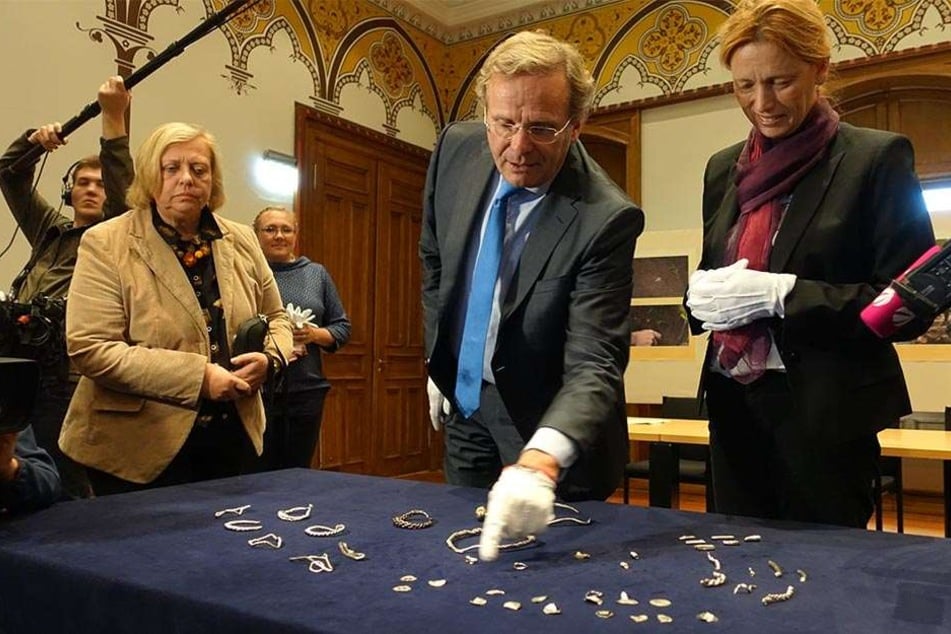 Der Leiter des Archäologischen Landesamts, Claus von Carnap-Bornheim (M.) und Kulturministerin Karin Prien (CDU, re) schauen sich den Silberschmuck an.