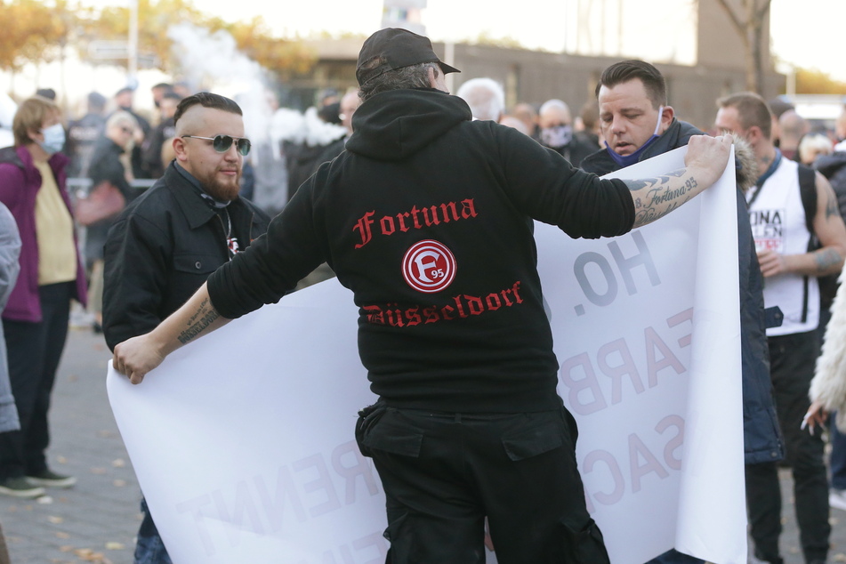 Demonstranten stehen auf dem Johannes Rau Platz neben Organisator Dominik Roeseler (r) bei einem Protest gegen die Corona-Maßnahmen.