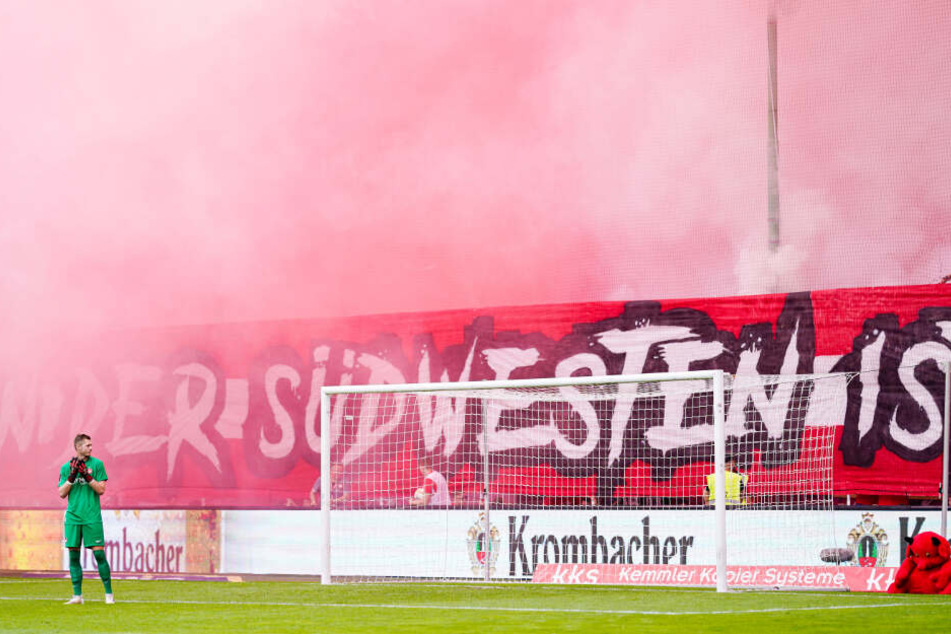 Kaiserslauterns Torwart Lennart Grill betrachtet den dichten weiß-roten Rauch auf Kaiserslauterns Fantribüne.