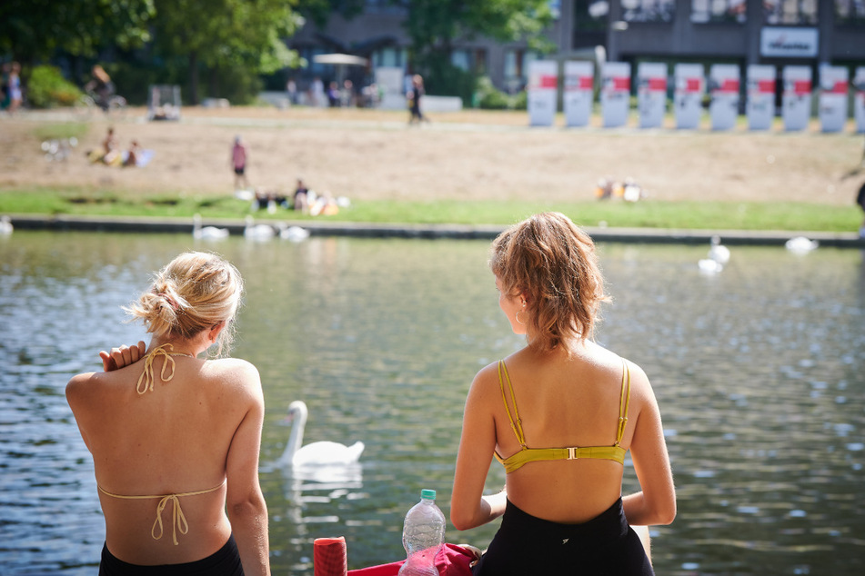 Zwei junge Frauen sitzen auf der Wiese am Landwehrkanal in der Sonne. Bereits das vergangene Wochenende brachte Temperaturen bis über 30 Grad.