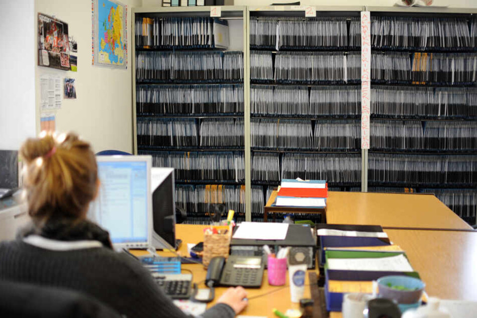 Eine Mitarbeiterin arbeitet vor Regalen voller Akten von Antragstellern in einem Amt. (Archivbild)