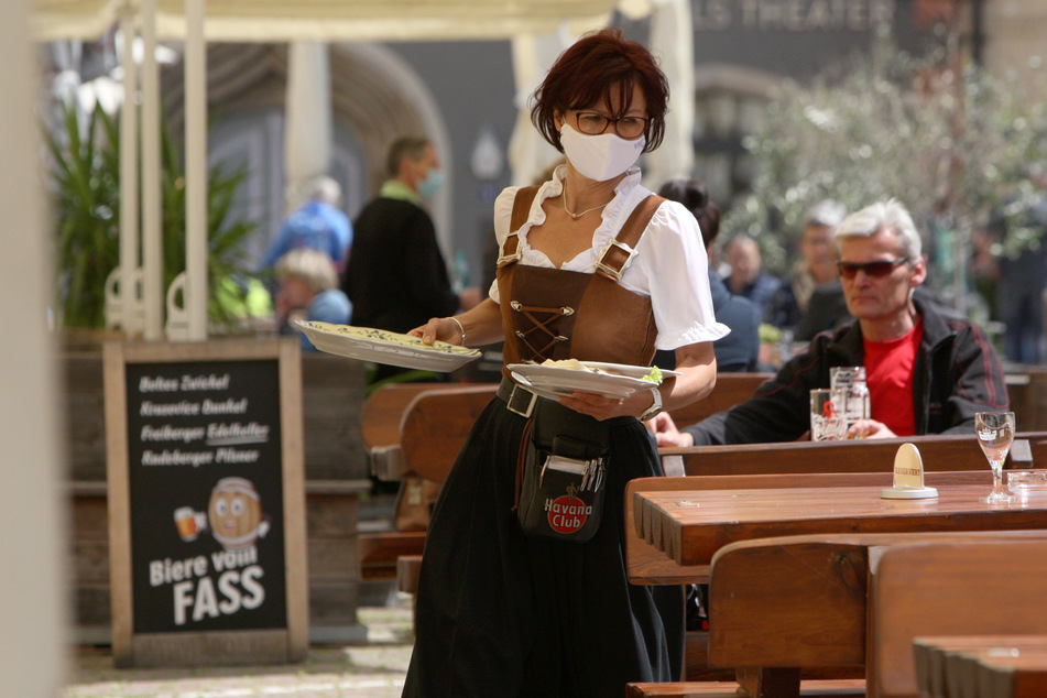 Eine Kellnerin mit Mundschutz bewirtet die Gäste vor der Gaststätte Ratsherrenstuben in Pirna.