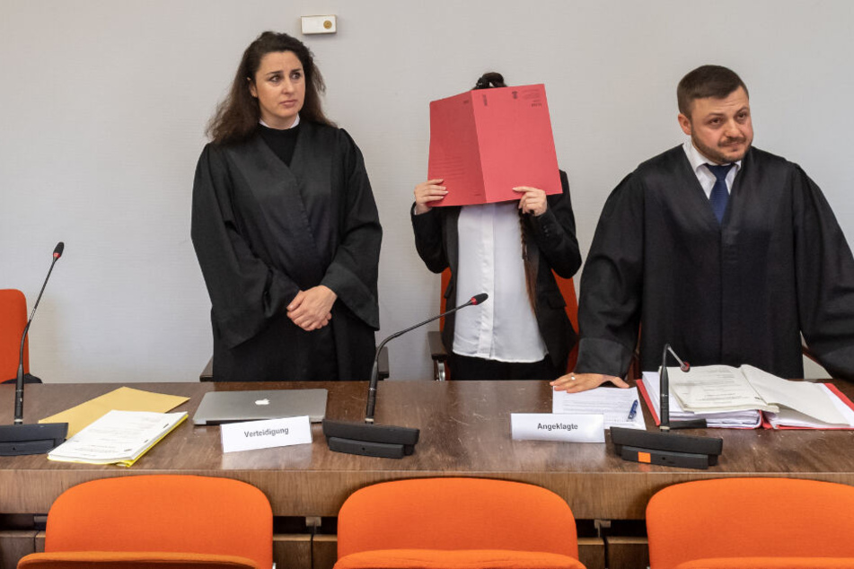 Archiv: Die Angeklagte (2.v.r) steht mit einem roten Aktendeckel vor ihrem Gesicht zu Prozessbeginn zwischen den Anwälten Sera Basay-Yildiz (l) und Ali Aydin (r) im Gerichtssaal.