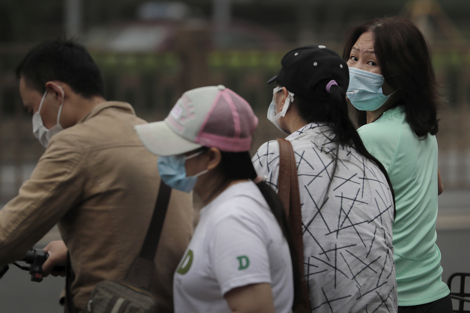 Menschen mit Mundschutz warten in Peking darauf, eine Straße zu überqueren. Neue Fälle von Coronaviren nehmen in der nordwestlichen Region Xinjiang in China extrem schnell zu.