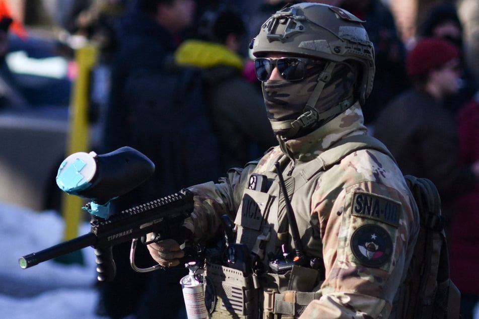 A federal officer stands guard as protestors gather while ICE operates in a residential neighborhood in Minneapolis, Minnesota, on January 13, 2026.