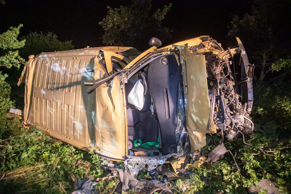Der völlig zerbeulte Transporter liegt neben der Fahrbahn auf der Beifahrerseite.