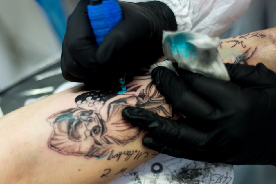 Eine Tätowiererin sticht einer Frau ein Tattoo am Unterarm.