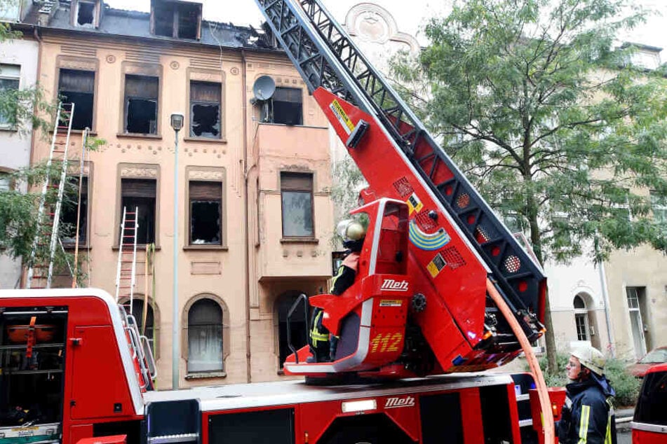 Feuerwehrleute untersuchen mit Hilfe einer Drehleiter das abgebrannte Haus.