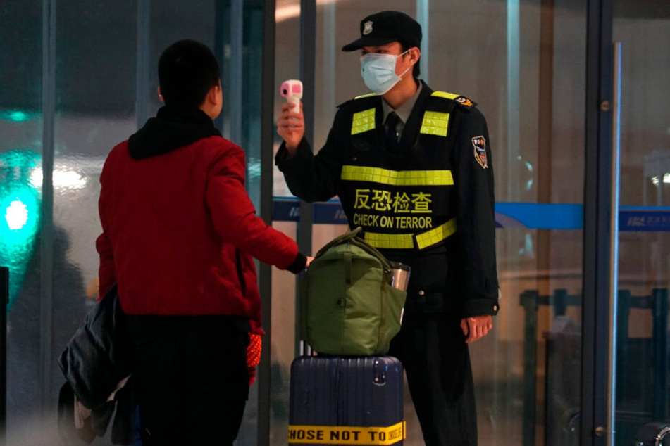 Ein Mitarbeiter des Flughafen Wuhan Tianhe International Airport trägt Mundschutz und misst bei einem Reisenden Temperatur.