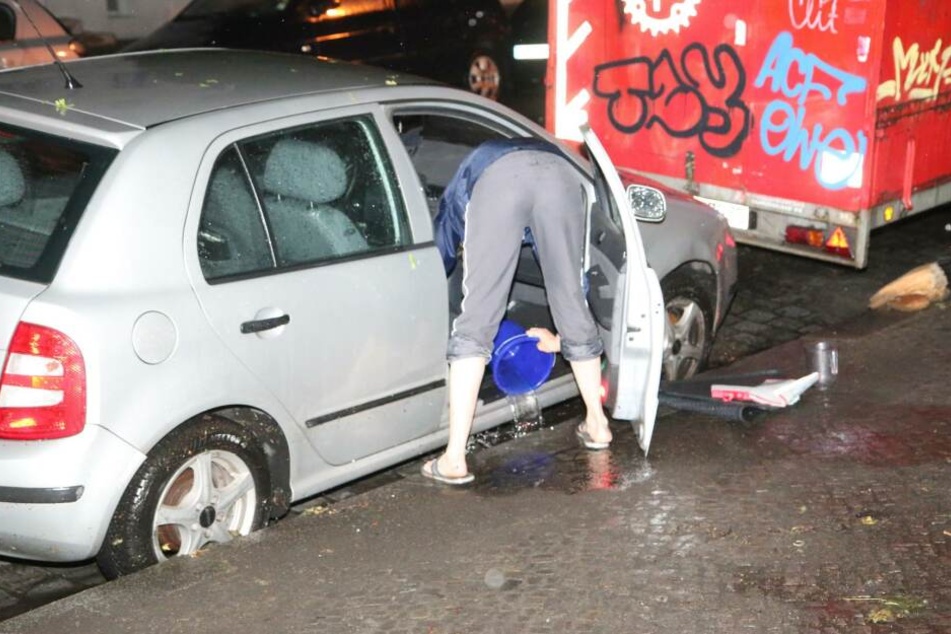 Auto-Besitzer versuchen ihre Wagen mit Eimern von den großen Wassermengen zu befreien.