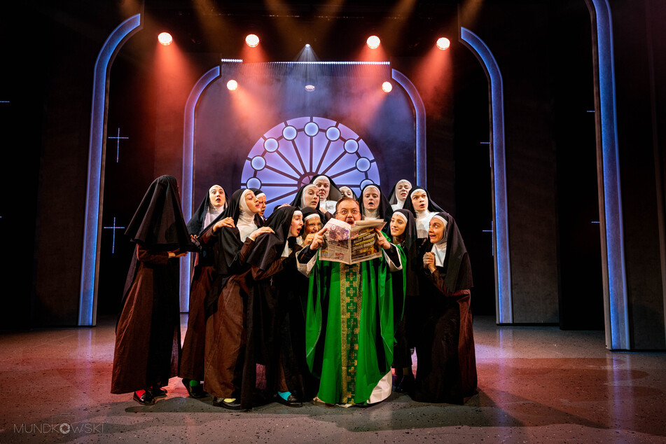 Monsignore Howard (in grün), gespielt von Dejan Drkic, präsentierte den Nonnen den positiven Artikel über ihre neuen Gesangseinlagen in der Kirche.