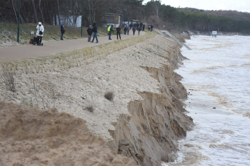 Menschen laufen auf einem Weg in Zempin am Meer entlang. Hier hat die Sturmflut ganze Küstenabschnitte abgetragen.