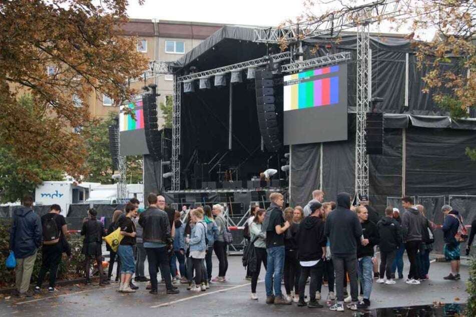 Konzertbesucher warten auf dem Parkplatz an der Johanniskirche hinter einer Absperrung vor der Bühne.