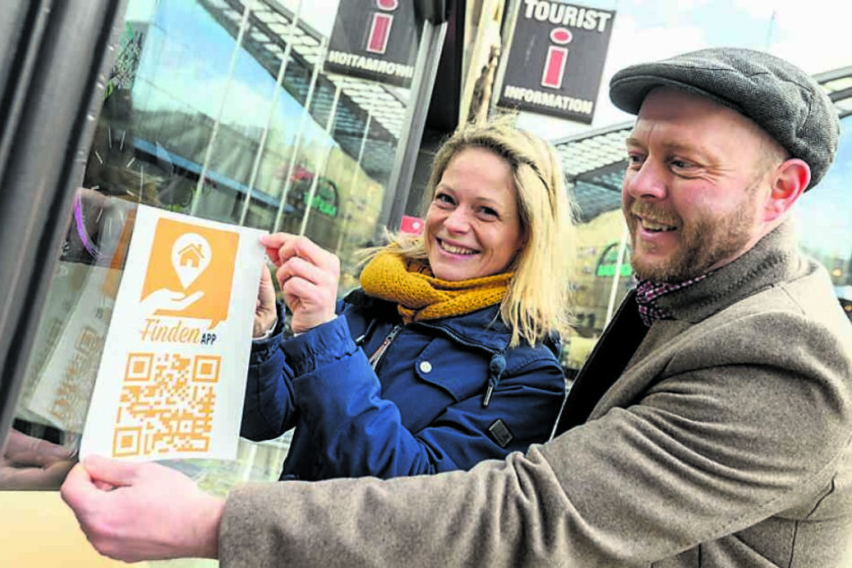 Susan Endler (38) von der CWE und Alexander Seidel (39) vom SFZ Förderzentrum bringen ein Hinweisschild für die "findenApp" an der Touristinformation an.