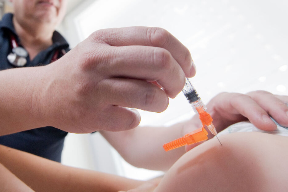 Ein Kinderarzt impft ein einjähriges Kind in den Oberschenkel mit dem Impfstoff Priorix (Lebendvirusimpfstoff gegen Masern, Mumps und Röteln).