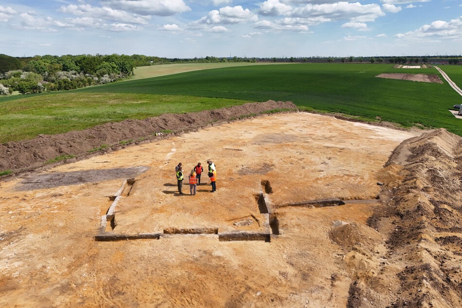 Archäologen stehen in Mitten einer Trapezanlage.