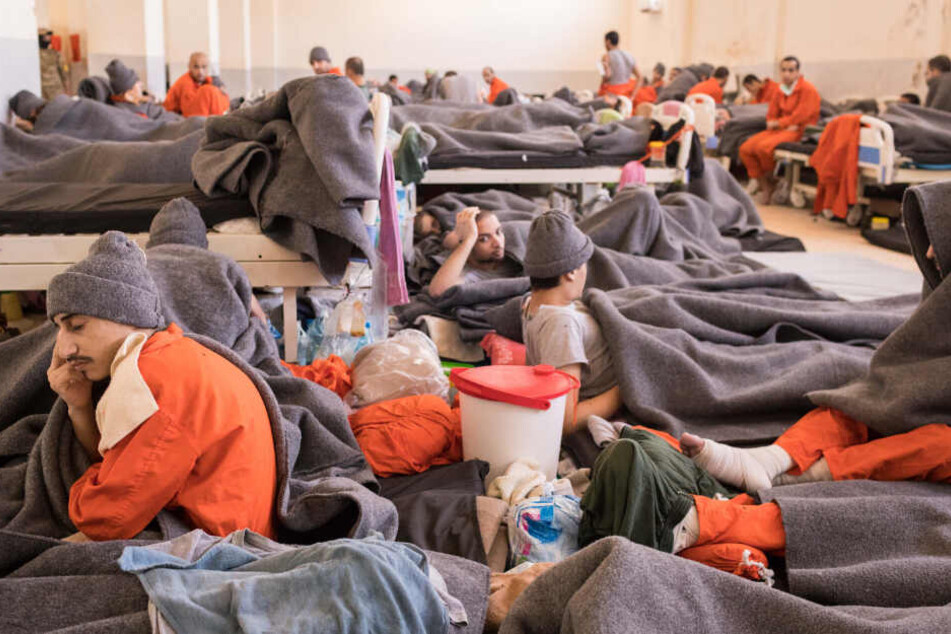 Zahlreiche Männer in orangenen Overalls sitzen und liegen in einem Raum.