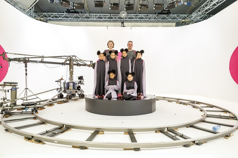 Schauspielerin und Schauspieler sowie die Kinderdarsteller am futuristischen Set, mit Schienen für die Kamerafahrt.