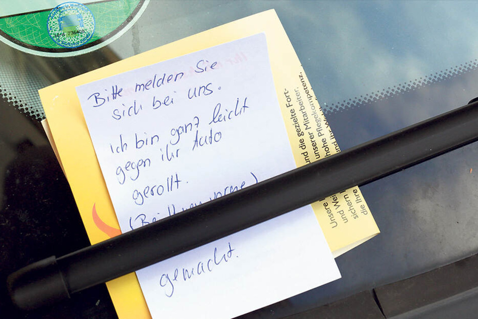 Ein Zettel mit der Aufschrift "Bitte melden Sie sich bei uns. Ich bin ganz leicht gegen ihr Auto gerollt", klemmt an einem PKW hinter einem Scheibenwischer.