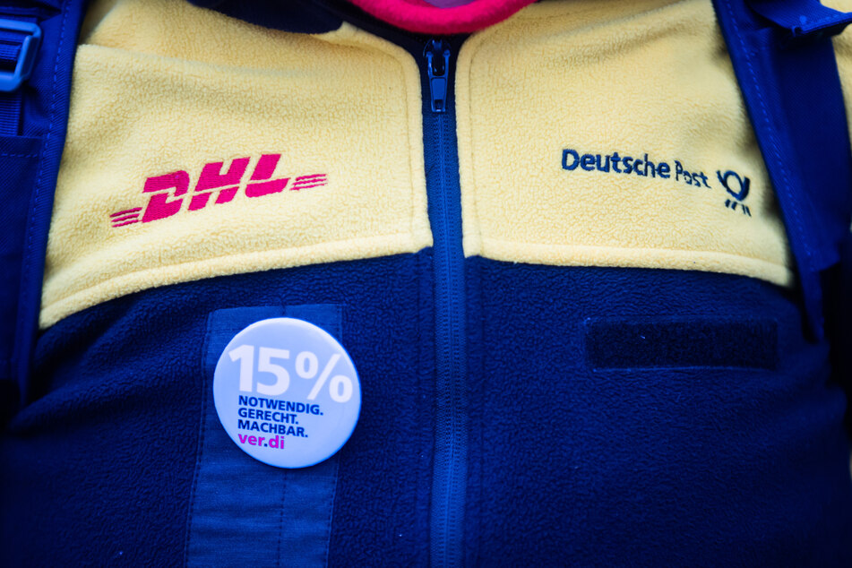 Eine Teilnehmerin eines Streiks von Post-Beschäftigten trägt an ihrer Dienstkleidung einen 15 %-Anstecker.
