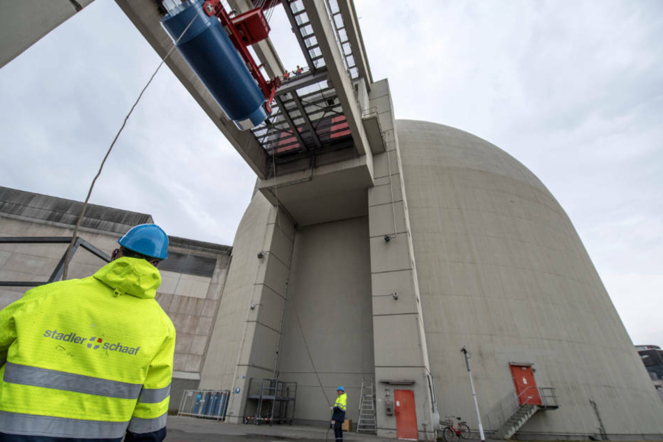 Mit Hilfe eines Schwerlastkranes heben Arbeiter einen blauen Castorbehälter in das Innere eines der Reaktorblöcke des Atomkraftwerk Biblis. (Archivbild)