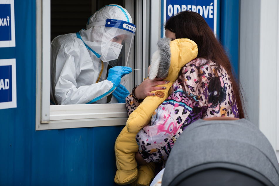 Ein Mitarbeiter des Gesundheitswesens in Schutzkleidung nimmt während der Corona-Massentests eine Nasenabstrichprobe von einem Kleinkind in Bratislava.