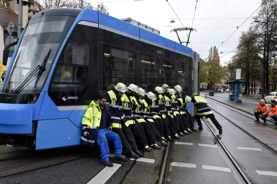 Die Feuerwehrleute stemmen sich gegen die entgleiste Tram, um sie zurückzuschieben.