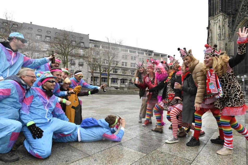 Eine Gruppe verkleideter Männer fotografieren eine weibliche Karnevalistengruppe vor dem Kölner Dom. Die Weiberfastnacht leitet den Beginn des Straßenkarnevals ein.