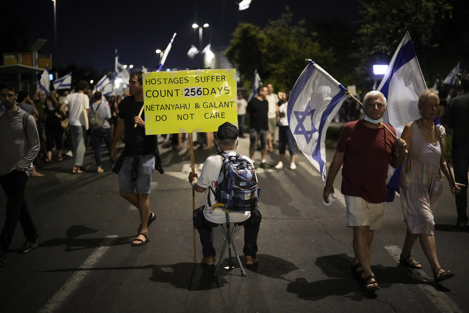 Menschen schwenken israelische Flaggen und Schilder während einer Demonstration gegen die Regierung.