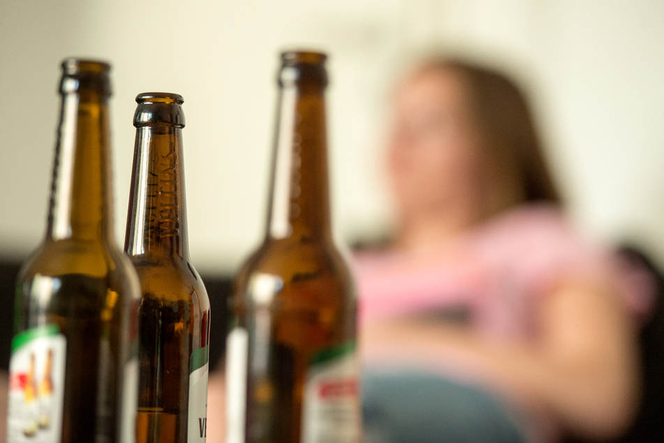Eine junge Frau sitzt hinter leeren Bierflaschen.