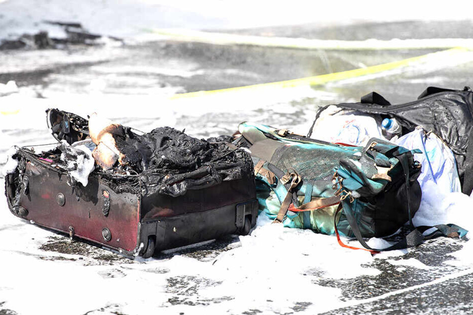 Taschen und Koffer liegen verkohlt neben dem Brandfahrzeug.