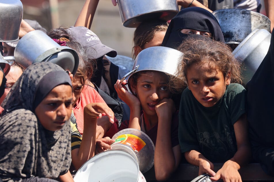 Palestinian women and children wait to receive food portions from a charity kitchen in Khan Younis in the southern Gaza Strip on August 27, 2025.