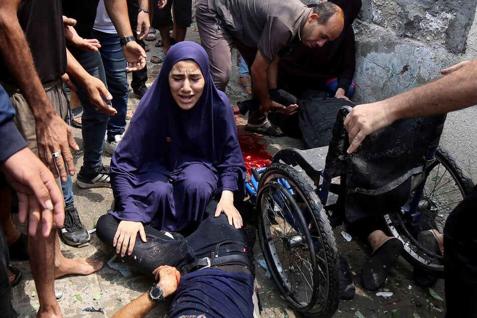 A Palestinian woman mourns while touching the body of a man killed in an Israeli airstrike on Gaza City on August 12, 2025.