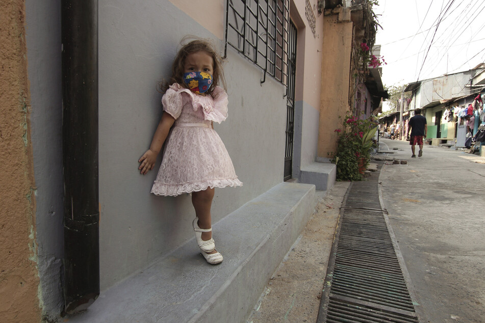 Eine Fünfjährige steht in der Papini-Gemeinde in San Salvador mit einer Mundschutzmaske vor ihrem Elternhaus.