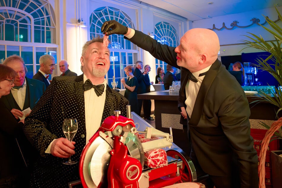 Caterer Roland Hess (r.) verköstigt Promi-Figaro Holger Knievel mit frisch geschnittenem Schinken.