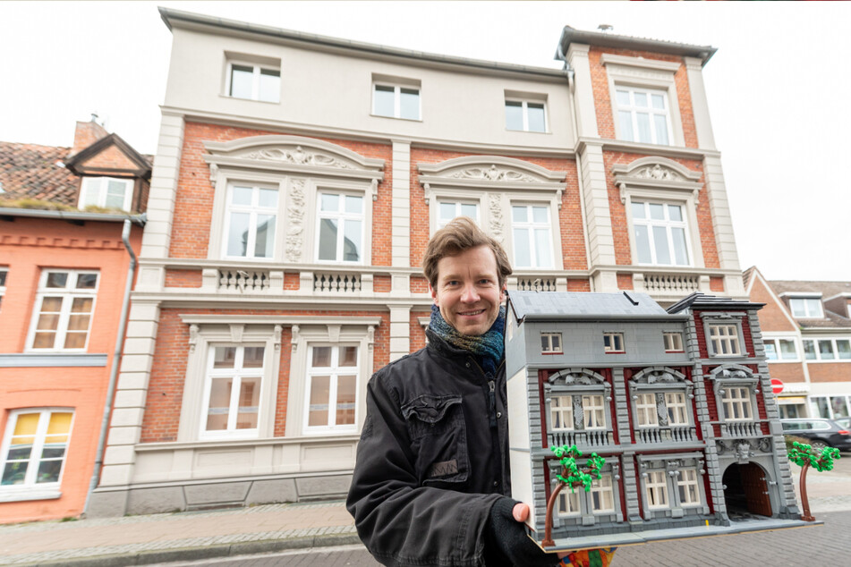 Benjamin Albrecht steht vor einem Lüneburger Gebäude mit einem Nachbau aus Legosteinen.