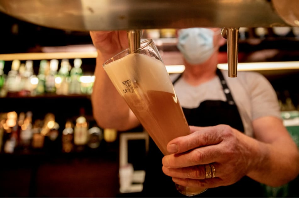 Ein Wirt mit Maske zapft in einer Kneipe im Berliner Bezirk Wilmersdorf Bier in ein Glas.