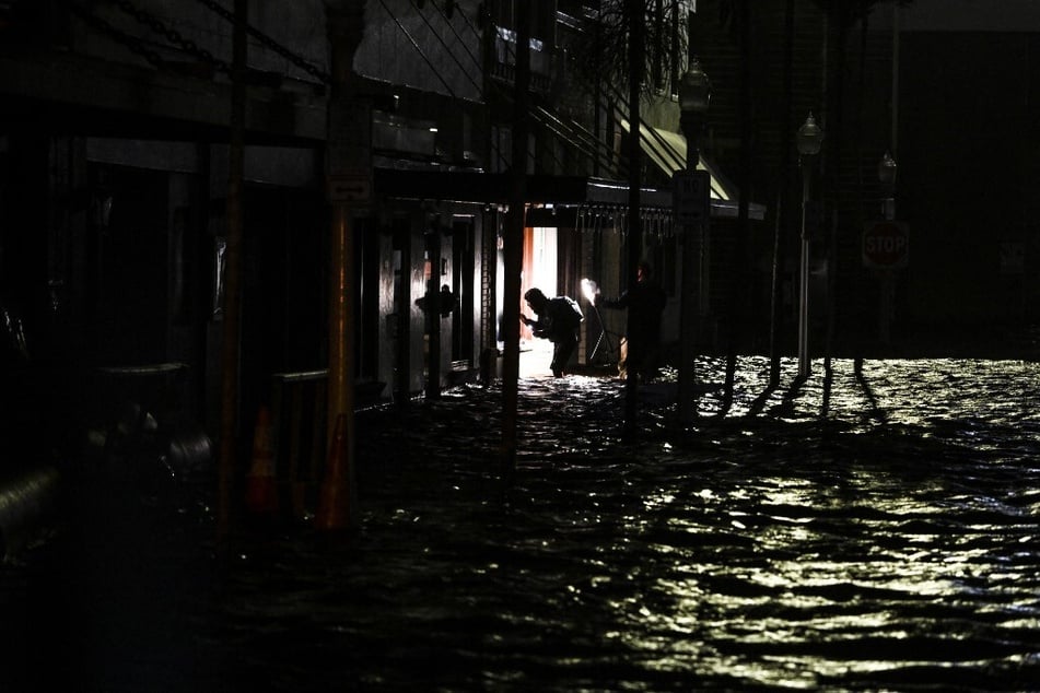 People use their phones to take photos and shine lights as they walk through water-flooded streets after Hurricane Milton made landfall in Fort Myers, Florida, on October 9, 2024.