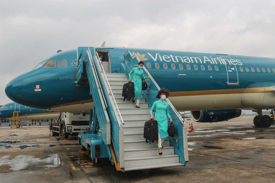 Besatzungsmitglieder von Vietnam Airlines, die Mundschutzmasken tragen, gehen am internationalen Flughafen Noi Bai mit Koffern in der Hand von Bord.