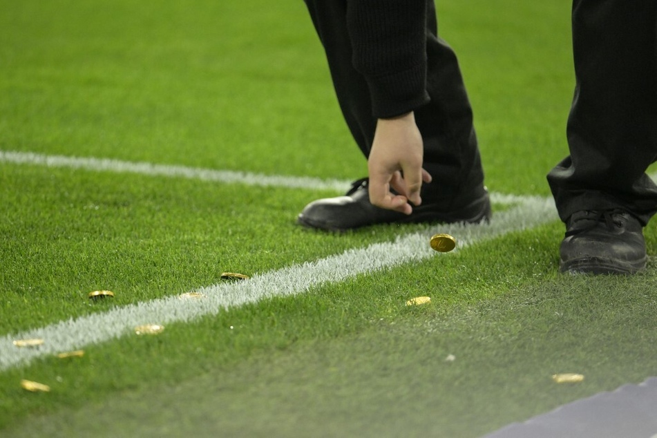 Ein Stadion-Mitarbeiter liest die Schoko-Münzen vom Rasen auf.