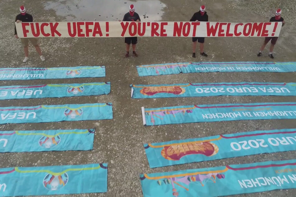 Vor insgesamt 22 offenbar selbst entwendeten Bannern zur Fußball-EM positionieren sich die Aktivisten und zeigen ein Transparent mit ihrer Botschaft an die UEFA.