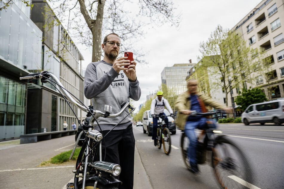 Falko Görres (42, Die PARTEI), Fahrradaktivist und Stadtverordneter im Frankfurter Römer, steht auf der Mainzer Landstraße und fotografiert für eine Anzeige ein Lieferservicefahrzeug, das auf dem Radweg parkt.