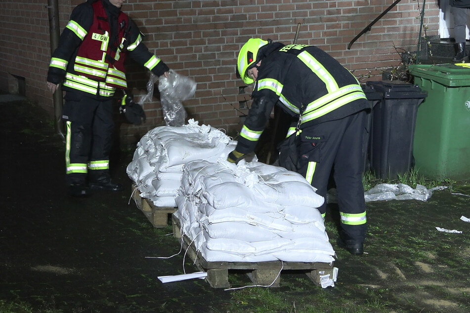 Einsatzkräfte der Feuerwehr legen Sandsäcke an einem Haus aus.