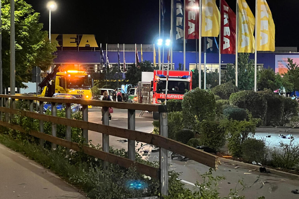 Einsatzkräfte sind nach dem Unfall auf dem IKEA-Parkplatz mit der Unfallaufnahme beschäftigt. Rechts im Bild ist der durchbrochene Zaun zu sehen.