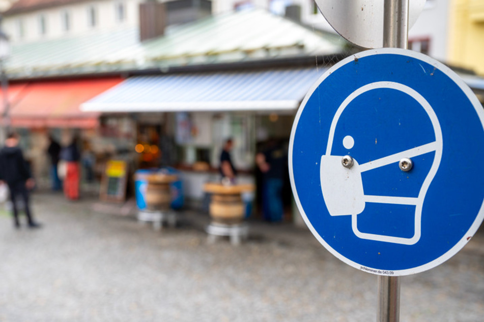 Ein Schild fordert am Münchner Viktualienmarkt zum Tragen einer Mund- und Nasen Bedeckung auf.